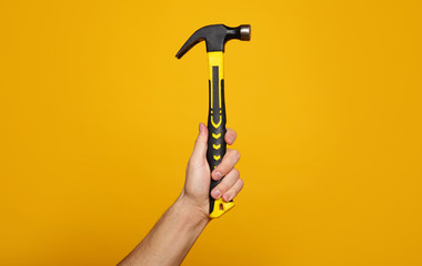 Carpenter hammer. Close-up photo of a hand holding a hammer on a yellow background. Home renovation...