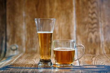 A glass and a mug of tasty beer stand on a brown background with cheese and nuts. Fragrant beer lit by beautiful light stimulates appetite.