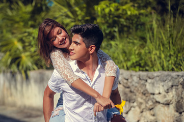 Smiling handsome young man carrying woman on his back doing piggyback and laughing outdoors. Happy smiling teenage couple having fun at summer park. Holidays, vacation, love and people concept