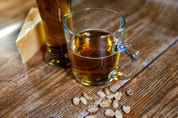 A glass and a mug of tasty beer stand on a brown background with cheese and nuts. Fragrant beer lit by beautiful light stimulates appetite.