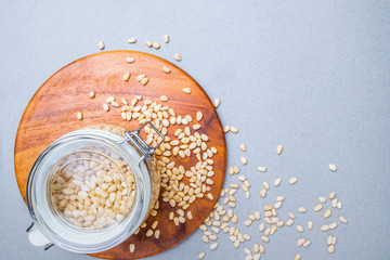 Glass jar with Siberian cedar nuts standing on a wooden stand on a gray background. Nuts scattered on the surface. Organic plant foods rich in vitamins, trace elements and energy. Copy space