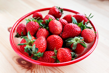 Strawberries in red bowl on wooden background.