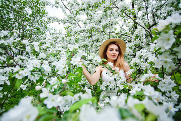 Beautiful teen redhead girl enjoying life in spring blossoming garden against blooming trees. Young dreamy thoughtful lady in nature at sunset. Springtime at countryside concept