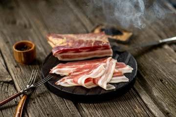 Salted bacon on wooden board with pepper fork knife smoke wooden texture cuisine daylight