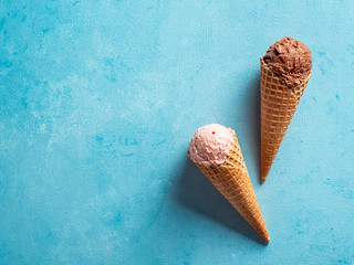 Various ice cream scoops in cones with copy space. Colorful ice cream in cones chocolate, strawberry, blueberry, pistachio or matcha, biscuits chocolate sandwich cookies on blue background. Top view