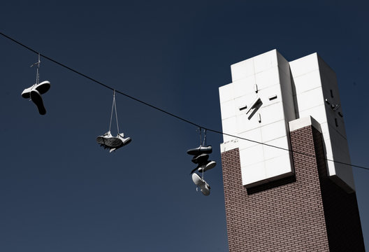 Sneakers Hanging On Cables In Working Class Neighborhood With Clock Tower