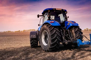 Foto op Plexiglas tractor in a field at sunset processes the field © Vladyslav