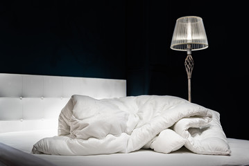 bed with pillows crumpled white warm blanket on a white bed against a background of dark walls