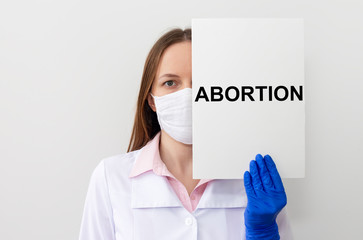 Doctor woman in protective mask and gloves holds a paper with text abortion