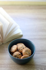 Bowl of chocolate chip cookies and open book on a table. Selective focus.
