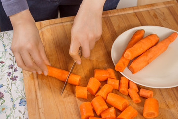 Kobieta w kuchni kroi marchewki na kawałki za pomocą noża. - obrazy, fototapety, plakaty