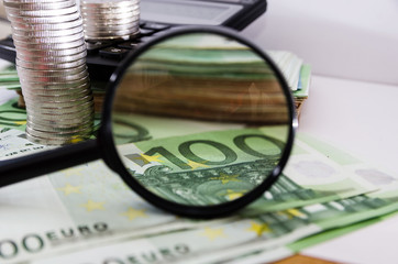 100 euros through a magnifier on a background of euro banknotes and coins.