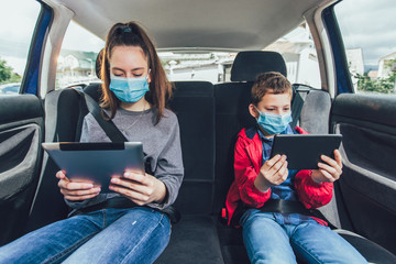 Kids wearing anti virus masks and using digital tablets in the car. Kids are travelling in car...