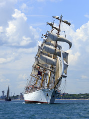 Fototapeta na wymiar White sailing ship with prominent sails against a blue sky with white clouds.