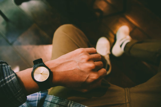 Young man sitting on chair wears a tartan shirt looking at his analog watch on his hand watching the time at the coffee shop. waiting for an appointment. Vintage tone