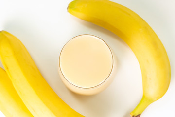 Banana smoothie, juice in a glass over white background, bananas in background. top view, selective focus