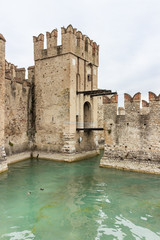 Obraz premium The water moat filled with water in front of the walls of the Castello Scaligero fortress, on Lake Garda in the Sirmione town in Lombardy, northern Italy