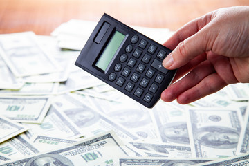 Calculator in hand on a background of dollars.
