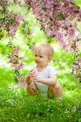 Close-up portrait of a 1-2 year old girl outdoors in a garden with pink flowers in the trees.