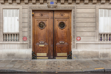 Two beautiful and decorative wooden doors on side of classic Paris building with wet sidewalk