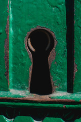 A rusty keyhole in an old cracky green metal door