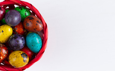 Colored quail eggs in red basket on white wooden table. Easter table setting. Spring holiday. Flat lay. Top view. Free space.