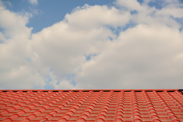 Red roof of a house on a blue sky with clouds