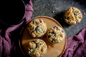 Blaubeeren-Muffins auf Holzscheibe mit dunklem Untergrund