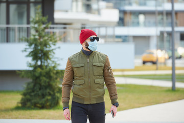 A man in a medical face mask to avoid the spread coronavirus holding his smartphone in a cozy...