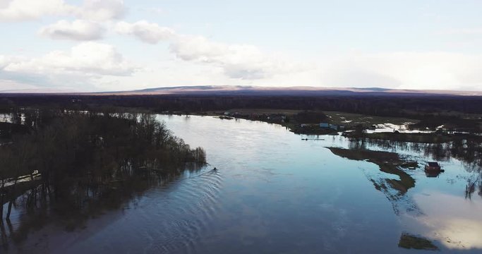 Three people on old powerboat floating on floodplain river / Evacuation from flooded area with submerged trees. Wide aerial drone shot.