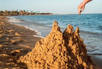 Sand castle made of sand by the hands of a child on the shore.Sea at sunset, white sand on the...