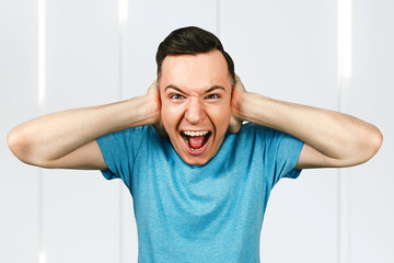 Young man covers ears and shout, dressed in a blue t shirt