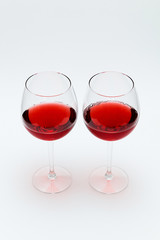 Two glasses of red wine stand on a white table.