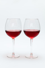 Two glasses of red wine stand on a white table.