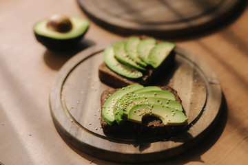 Avocado sandwich on dark rye bread made with fresh sliced avocados from above. Vegan sandwich on wooden board sprinkled with sesame seeds