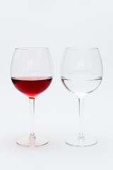 Two glasses on a white table. One is filled with red wine, the other is water.