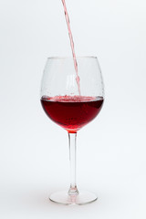 Red wine is poured into a large glass on a white background
