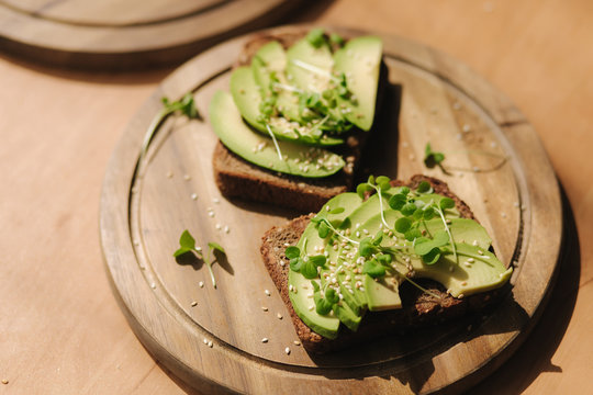 Avocado toast on wooden boadr. Vegetarian food concept. Fresh food at home. Sandwich with avocado and rye toasted bread, sesame seeds and mustard seedings