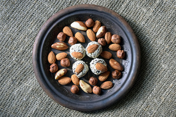 Various nuts are laid out in a brown handmade clay plate placed on a gray burlap.