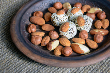 Various nuts are laid out in a brown handmade clay plate placed on a gray burlap.