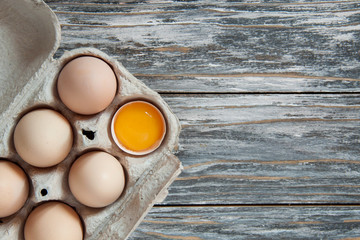 Farm chicken eggs in a cardboard box on a gray wooden table. Organic food. View from above