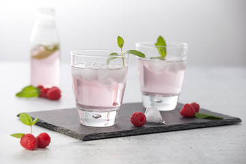 Glasses of raspberry infused water  with raspberries, ice and fresh mint leaves  on concrete background stone strong light with glass shadows. Copy space. 