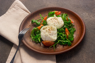 Poached eggs on lettuce and arugula, on a clay plate. Dark background