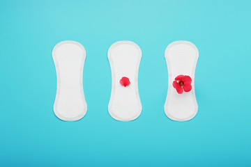 Sanitary pads in a row with a red flower on a blue background. The concept of critical days, stages of the menstrual cycle.