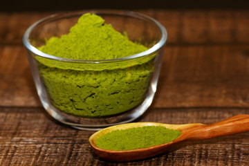Green tea matcha in a glass bowl and a spoon on a brown wooden background close-up. Matcha in a wooden spoon.