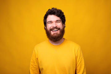 Simple portrait of a smiling bearded man in a positive mood on yellow background.