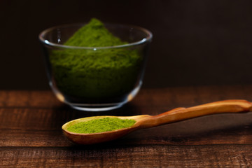 Green tea matcha in a glass bowl and a spoon on a brown wooden background close-up. Matcha in a wooden spoon.