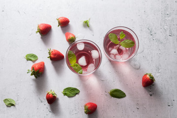 Naklejka na ściany i meble Glasses of strawberry infused water with strawberries, ice and fresh mint leaves on concrete background stone strong light with glass shadows. Copy space. Flatlay, top view.