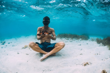 Freediver man with hold starfish and relax over sandy bottom in blue sea