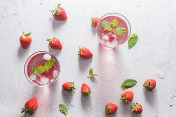 Glasses of strawberry infused water  with strawberries, ice and fresh mint leaves  on concrete background stone strong light with glass shadows. Copy space. Flatlay, top view.